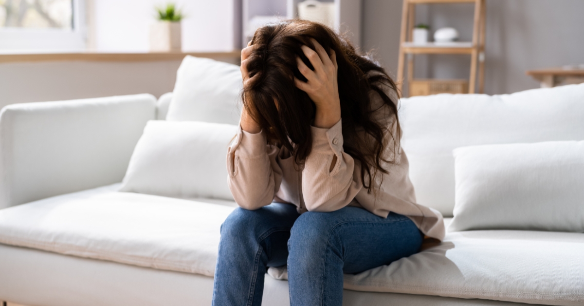 A teenage girl sitting on a couch, holding her head in distress, depicting the struggles of Teen OCD.